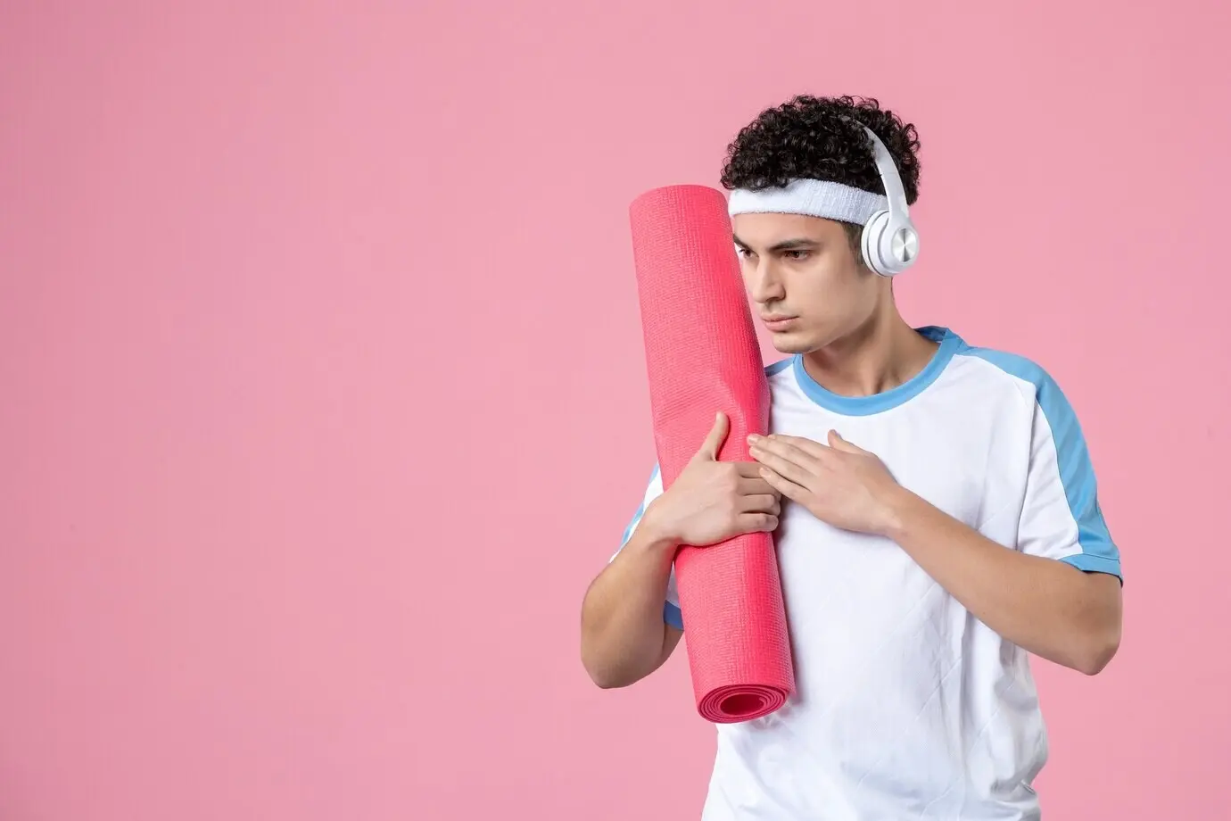 Вид спереди: молодой мужчина в спортивной одежде на фоне розовой стены.